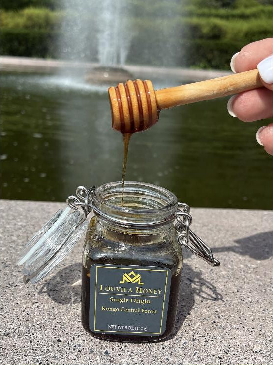 Honey pouring from a wooden dipper into the open Louvila jar